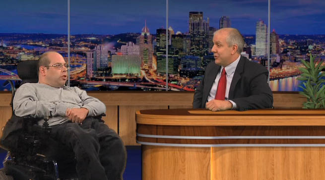 Photo of TV setting with a man in a wheel chair chatting with a talk show host